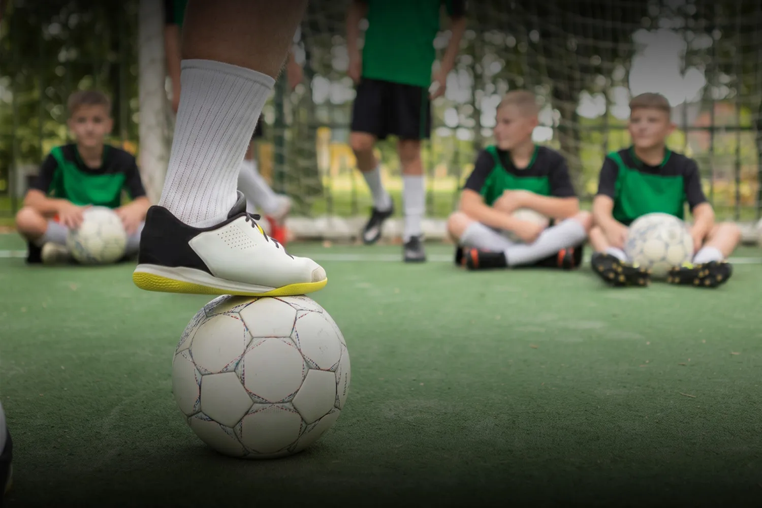 Niños de Baby Fútbol sentados en la cancha mientras un jugador apoya el pie sobre la pelota