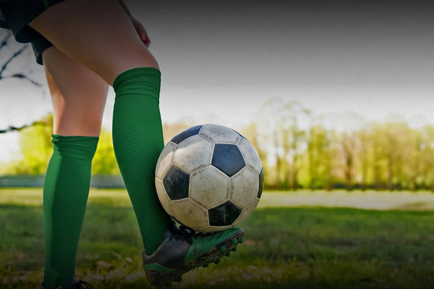 Jugadora de fútbol femenino con medias verdes controlando la pelota en una cancha de césped
